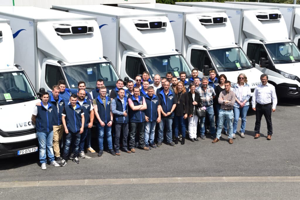 Équipe A.Z.P./CABRERO & camions frigorifiques Iveco Équipe souriante d'une vingtaine d'employés en gilets bleus devant des camions frigorifiques blancs Iveco, FRCX, Carrier, plaque FG-074-FD.